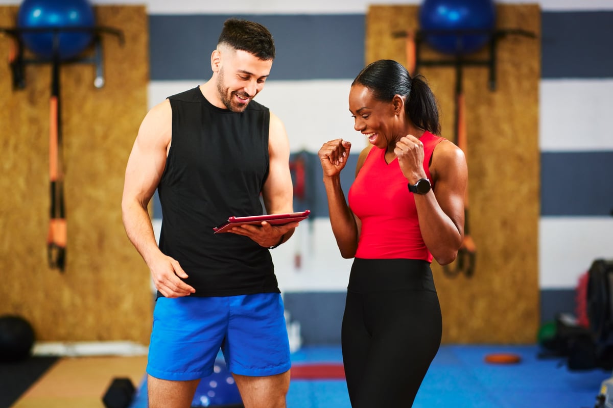 Personal trainer showing workout results on tablet to client in modern gym
